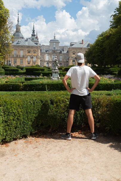 young teenager with a cloth visor with a white T-shirt and black shorts in the gardens of La Granja de San Ildefonso Palace 18th century Royal Palace in the province of Segovia in Spain on a summer - Photo, Image
