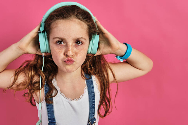 A little girl posing with headphones on a pink background - Foto, afbeelding
