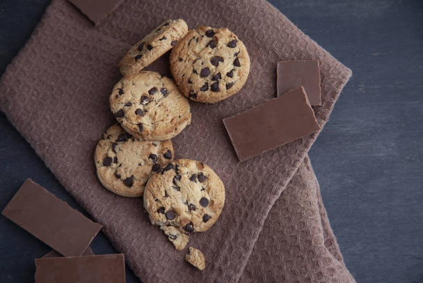 A top view shot of yummy cookies and a bar of chocolate on a brown towel - Fotoğraf, Görsel