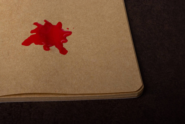 Gros plan d'une tache de peinture rouge sur du papier artisanal sur une surface brune sous les lumières - Photo, image