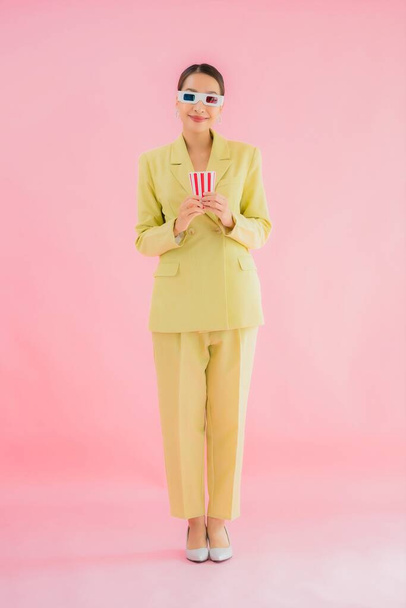 Porträt schöne junge asiatische Frau mit 3D-Brille und Popcorn bereit für Film auf farbigem Hintergrund ansehen - Foto, Bild