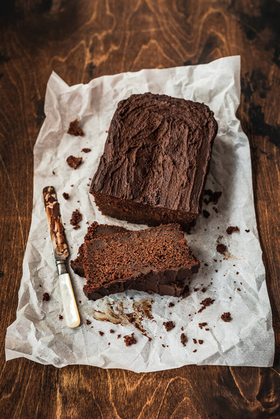 Sliced chocolate loaf cake and a knife on baking paper on dark wooden background - Fotografie, Obrázek