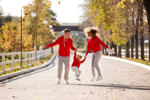 père et mère tiennent la petite fille par les mains et marchent dans le parc d'automne, la famille heureuse s'amuse à l'extérieur. la fête des pères, des mères et des bébés. focus sélectif. - Photo, image
