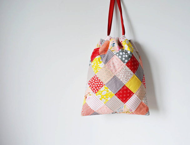 Colorful patchwork drawstring bag and white wall - Фото, изображение