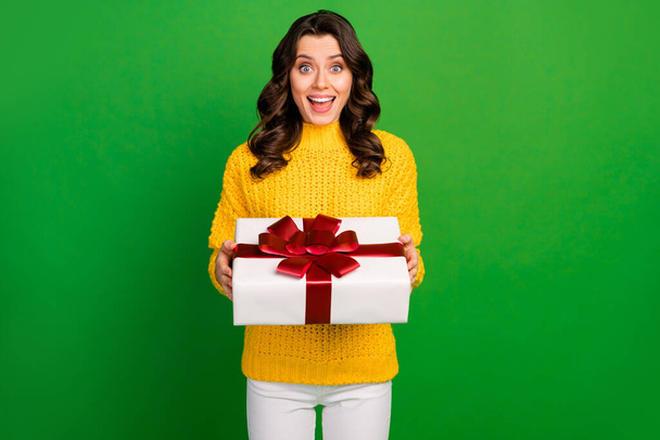 Photo of funny pretty lady hold big paper box with red bow birthday party gift from boyfriend wear knitted yellow sweater white trousers isolated vibrant green color background - Фото, изображение