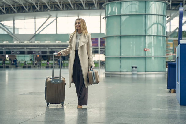 Positiva mujer rubia encantada sosteniendo su equipaje - Foto, Imagen