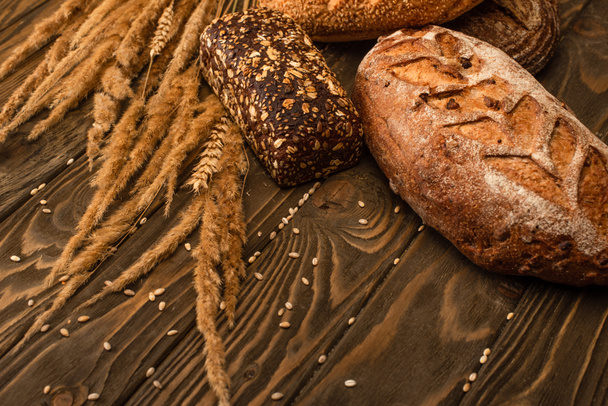 fresh baked bread loaves with spikelets on wooden surface - Foto, afbeelding