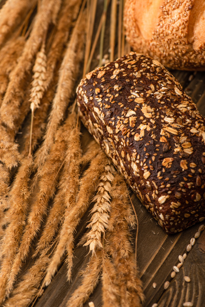 close up view of fresh baked bread loaves with spikelets on wooden surface - Fotó, kép