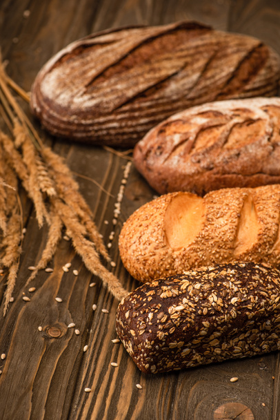 selective focus of fresh baked bread loaves with spikelets on wooden surface - Фото, зображення
