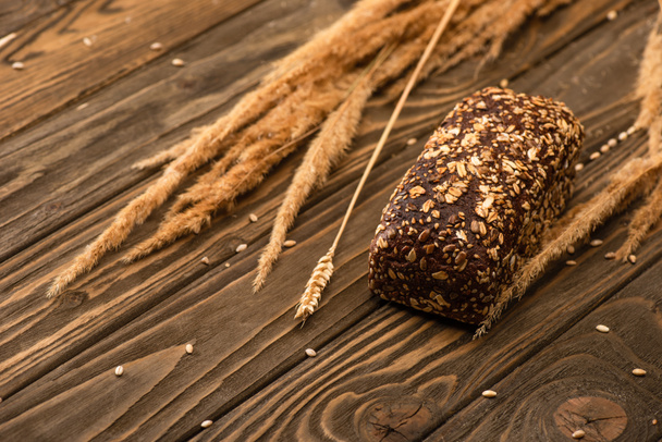 selective focus of fresh baked bread loaf with spikelets on wooden surface - Photo, Image
