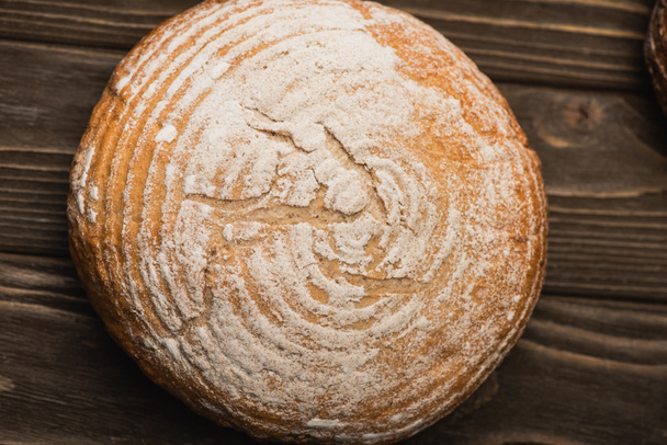 vrchní pohled na čerstvě upečený bílý bochník chleba na dřevěném povrchu - Fotografie, Obrázek