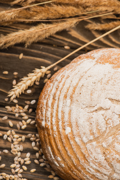 selective focus of fresh baked bread loaf with spikelets on wooden surface - Foto, immagini