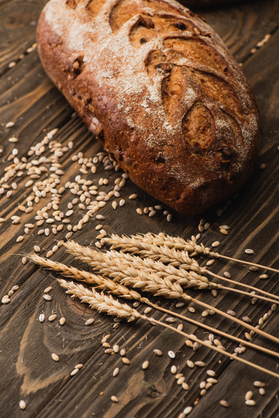 fresh baked bread loaf near spikelets on wooden surface - Foto, immagini
