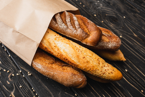 fresh baked baguette loaves in paper bag on wooden surface - Fotoğraf, Görsel