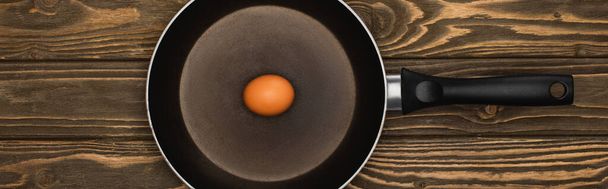 top view of raw chicken egg in frying pan on wooden surface, panoramic shot - Foto, immagini