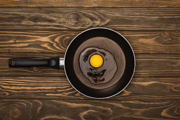 вид сверху на свежее разбитое куриное яйцо в сковороде на деревянной поверхности - Фото, изображение