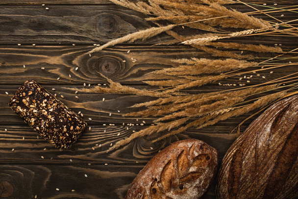 top view of fresh baked bread loaves with spikelets on wooden surface - Foto, afbeelding