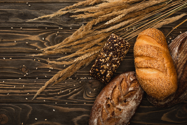 top view of fresh baked bread loaves with spikelets on wooden surface - 写真・画像