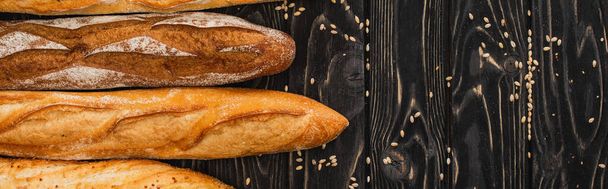 top view of fresh baked baguette loaves on wooden black surface, panoramic shot - Fotoğraf, Görsel