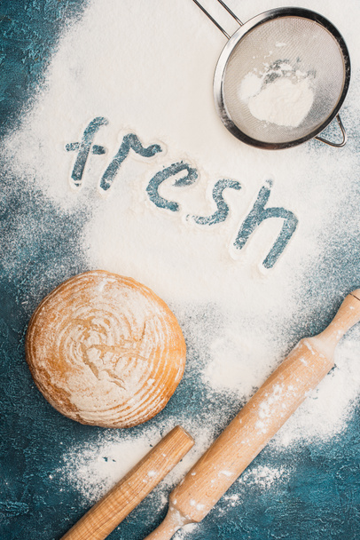 vista superior de pan recién horneado pan cerca de rodillo, tamiz y palabra fresca en la harina - Foto, imagen