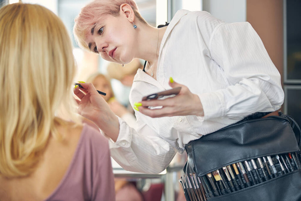 Geconcentreerde stylist doet make-up voor haar cliënt - Foto, afbeelding