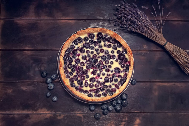 Rustic shortbread pie with blueberries in sour cream filling on a wooden background and a bouquet of dried lavender. Flatley top view - Φωτογραφία, εικόνα