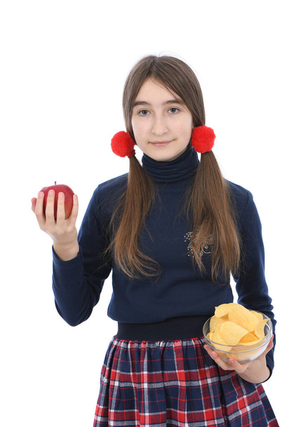 Pre-adolescent meisje weegt kommen vol chips en rode appel. Geïsoleerd op witte achtergrond. Hoge resolutie foto. Volledige scherptediepte. Concept van het kiezen van gezond en ongezond voedsel - Foto, afbeelding