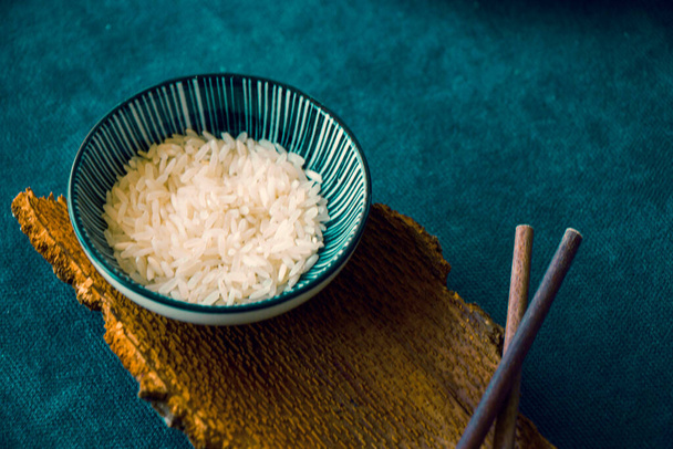Asian tableware, raw rice, bowl and chopsticks, wooden material, ceramic bowl. Seeds of rice. - Foto, imagen