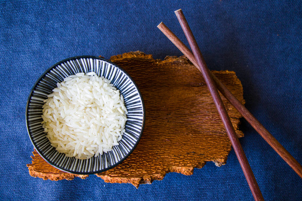 Азиатская посуда, сырой рис, миска и палочки для еды, деревянный материал, керамическая чаша. Семена риса. - Фото, изображение