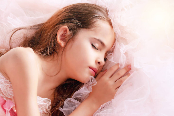 Adorable cute little girl brown long hair lying on pink fabric. Top view lovely kid sleeping relax on her dress. Tone pink filter.  - Φωτογραφία, εικόνα