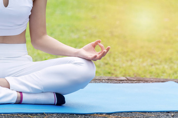 Mavi hasırda oturmuş parkta temel asma yogası yapan hareketli genç bir kadın. Rahatlayın, kadınlar yoga ve doğa ile egzersiz yaparlar. Sağlıklı egzersiz kavramı. - Fotoğraf, Görsel