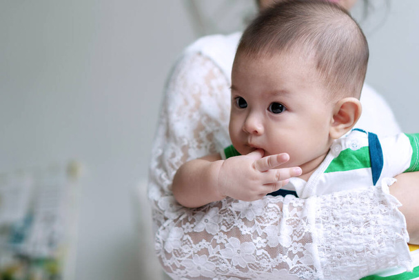 Lähikuva muotokuva aasialainen söpö poika vauva imee sormeaan, kun äiti kuljettaa makuuhuoneessa. Suhde ja rakkaus elämäntapa äitienpäivä käsite. - Valokuva, kuva