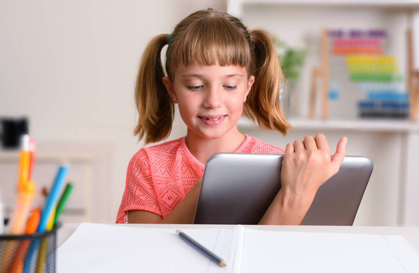 Happy girl studying at home desk taking distance lessons using a tablet - 写真・画像