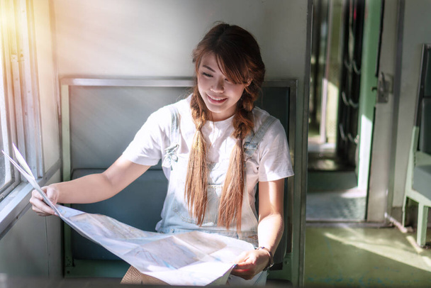 Woman tourist travel holding map in train near window. Traveler young girl expressing positivity hold generic map navigation sitting on the train looking map in her hands. Backpacker adventure concept - Фото, зображення