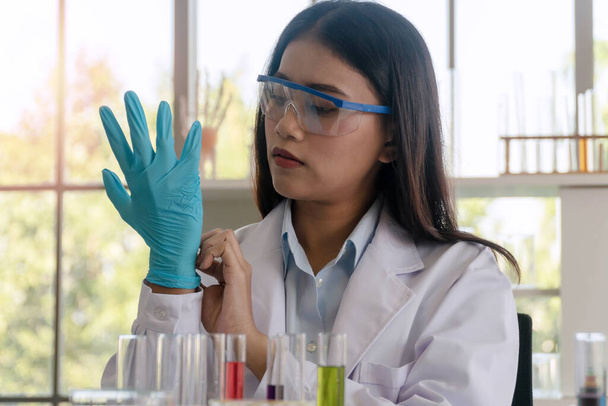 研究室で研究しながら、科学者や実務家の若い女性は青いラテックス手袋で彼女の手を置く.  - 写真・画像