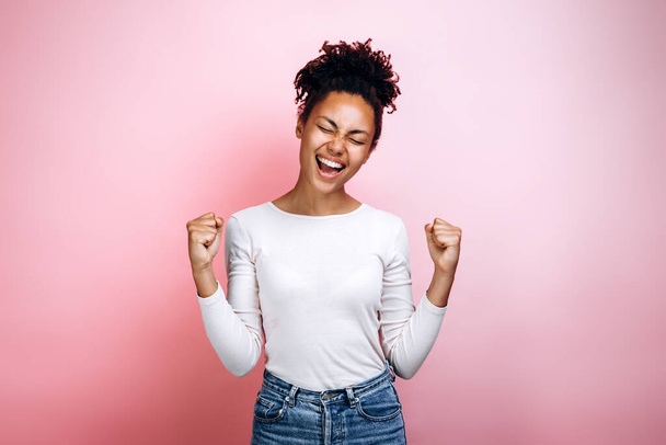 Overjoyed afro-amerikai Y-generációs lány elszigetelt rózsaszín stúdió háttér diadal kap jó hír. Nyertes koncepció - Fotó, kép