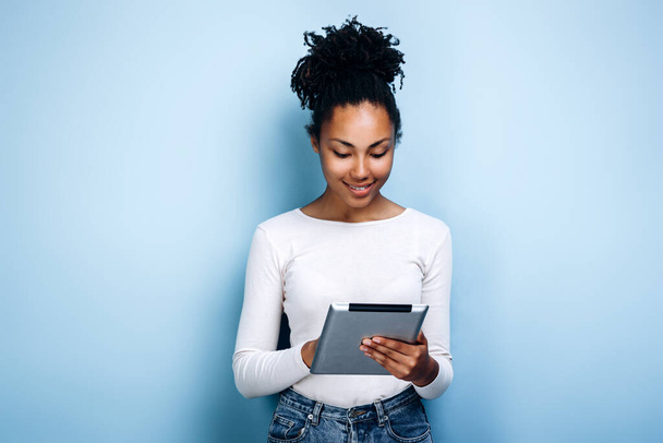 Business girl uses a tablet on a background of a blue wall - Fotoğraf, Görsel