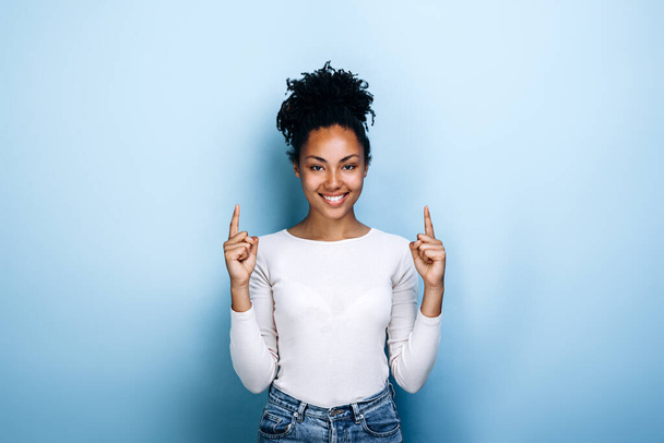 Positive, pretty, young girl showing thumbs up on a blue background - 写真・画像