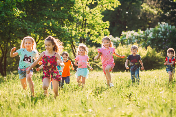 Large group of kids, friends boys and girls running in the park on sunny summer day in casual clothes . - Foto, imagen
