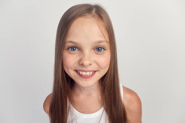 Veselá dívka v bílém tričku úsměv dlouhé vlasy close-up světlo pozadí oříznuté - Fotografie, Obrázek