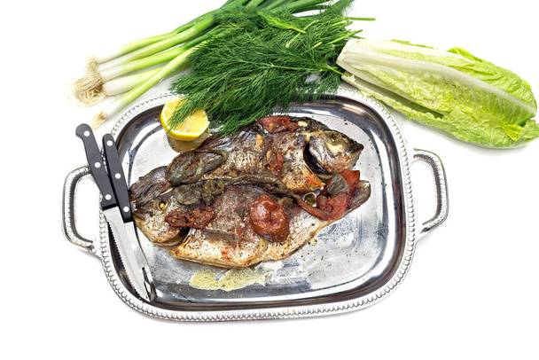 Seafood. Two, big, baked gilt-head bream (Sparus aurata) with vegetables on a plate close-up, on a white background - Photo, Image