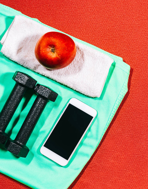 Az egészséges életmód jellemzői: alma, sporteszközök, kézi súlyok, sporting piros szőnyegen sportoláshoz a háttérben. Lapos nézet fénymásoló felülettel. - Fotó, kép