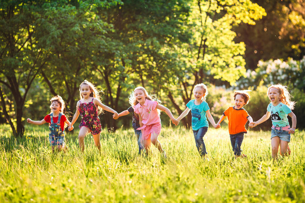Large group of kids, friends boys and girls running in the park on sunny summer day in casual clothes . - Foto, afbeelding
