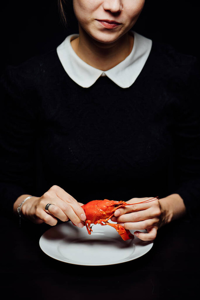 girl boiled crayfish in the hands on a white plate on a black background - Фото, изображение