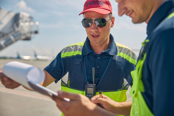 İniş sonrası kontrol listelerini inceleyen odaklanmış iki havaalanı çalışanı - Fotoğraf, Görsel