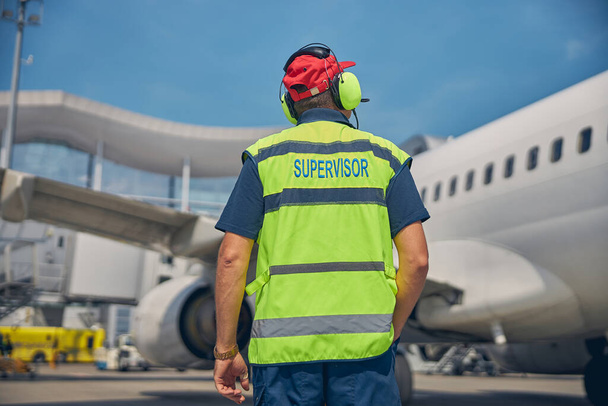 Сотрудник аэропорта смотрит на припаркованный самолет - Фото, изображение