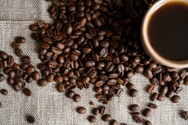 Coffee cup with roasted coffee beans on linen background. Mug of black coffe with scattered coffee beans. Fresh coffee beans. - Фото, зображення