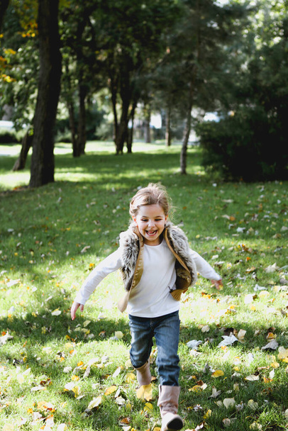 Happy little girl at autumn park wearing waistcoat. Childhood, happiness and season concept  - Foto, afbeelding