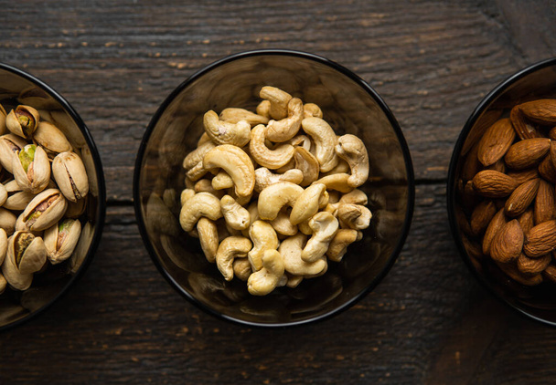 Almond, pistachio and cashew in a small plates which standing on a black table. Nuts is a healthy vegetarian protein and nutritious food. - Foto, Imagem