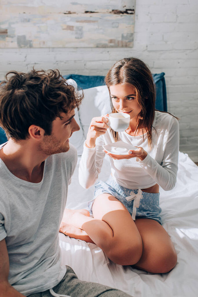 Young woman drinking coffee and looking at boyfriend - Фото, зображення